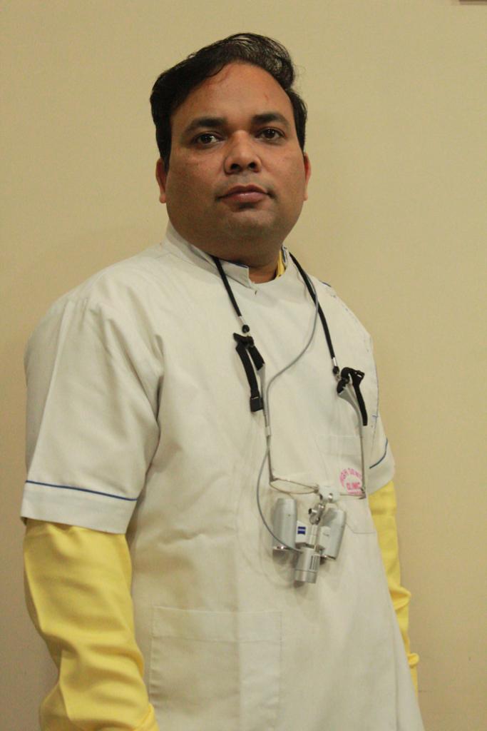 Dr. Pradeep Singh, experienced Indian dentist in his 50s wearing white medical coat and stethoscope, smiling warmly in modern dental clinic